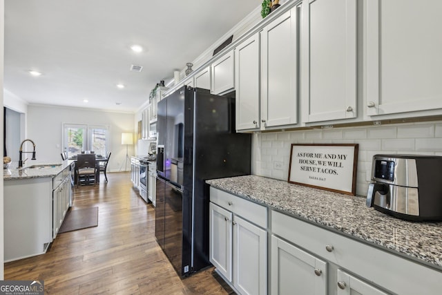 kitchen with sink, decorative backsplash, stainless steel range, light stone counters, and black fridge