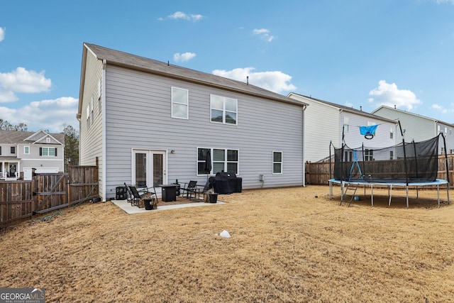 rear view of property with a fire pit, a lawn, a fenced backyard, a trampoline, and a patio area