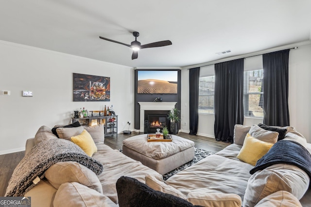 living area with visible vents, ornamental molding, wood finished floors, and a glass covered fireplace