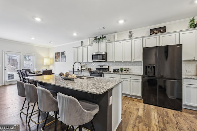 kitchen with light stone counters, stainless steel appliances, ornamental molding, a sink, and wood finished floors