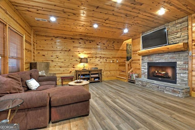 living room featuring wood-type flooring, a stone fireplace, wooden ceiling, and wood walls