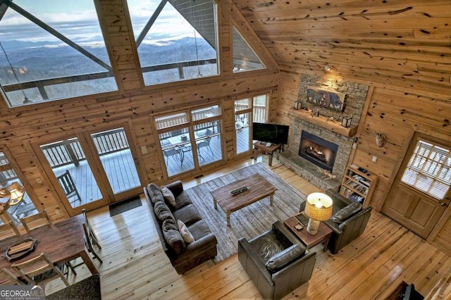 living room with high vaulted ceiling, wooden walls, a fireplace, and light hardwood / wood-style flooring