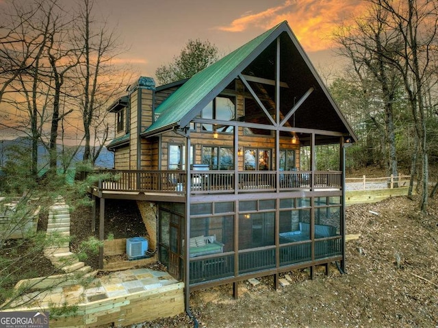 back house at dusk with cooling unit and a sunroom