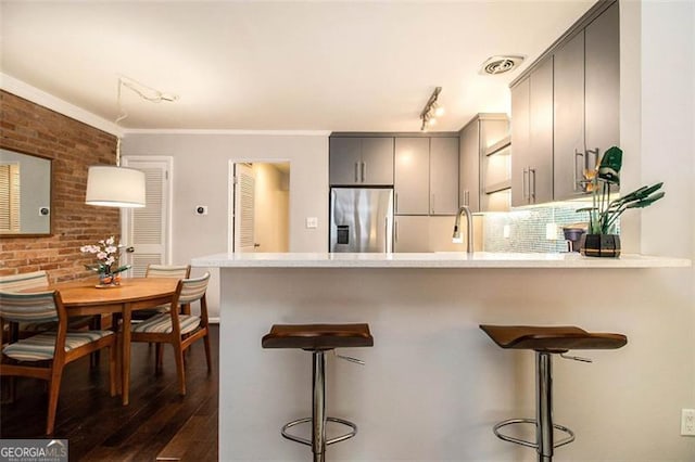 kitchen featuring a breakfast bar area, crown molding, stainless steel fridge with ice dispenser, gray cabinets, and kitchen peninsula