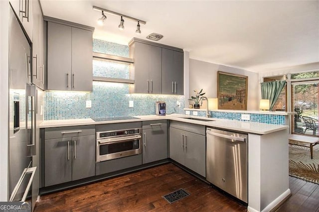 kitchen with sink, gray cabinetry, dark hardwood / wood-style floors, kitchen peninsula, and stainless steel appliances