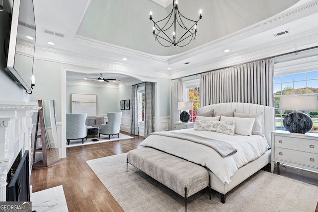 bedroom featuring a tray ceiling, hardwood / wood-style flooring, crown molding, and a premium fireplace