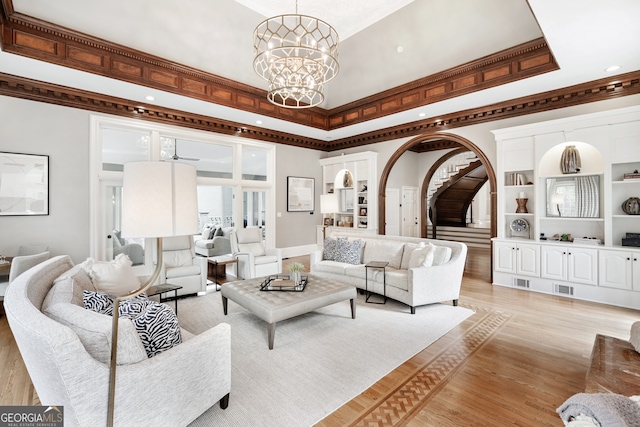 living room with crown molding, a tray ceiling, a chandelier, and light wood-type flooring