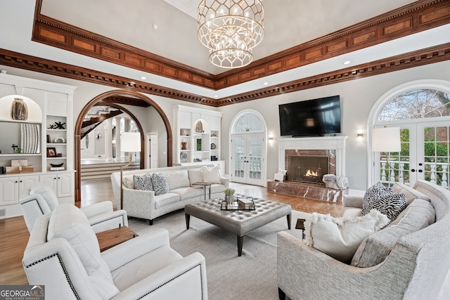 living room with a towering ceiling, a high end fireplace, french doors, a chandelier, and light wood-type flooring