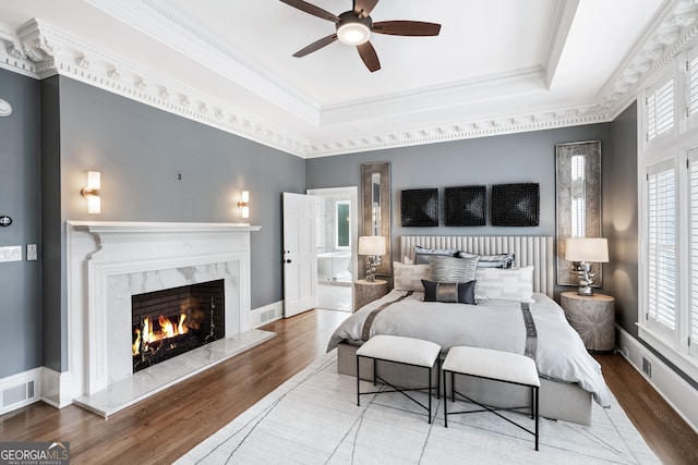 bedroom with ensuite bathroom, a fireplace, wood-type flooring, a tray ceiling, and crown molding