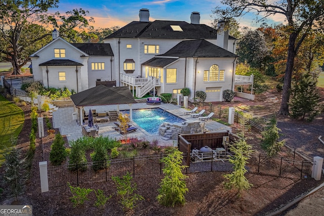 back house at dusk featuring a patio, a balcony, outdoor lounge area, a swimming pool with hot tub, and pool water feature