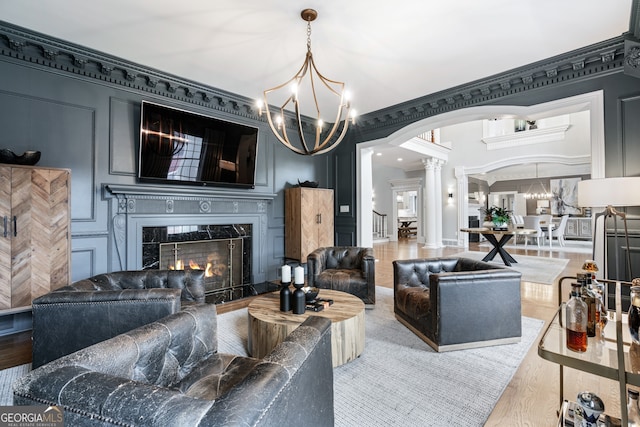 living room with decorative columns, wood-type flooring, a notable chandelier, a high end fireplace, and crown molding