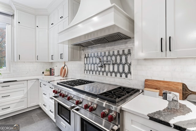 kitchen featuring double oven range, custom range hood, white cabinets, and backsplash