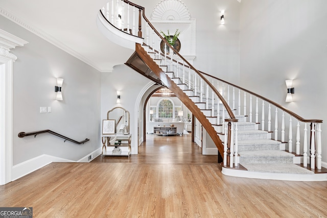 staircase featuring crown molding, wood-type flooring, and a high ceiling