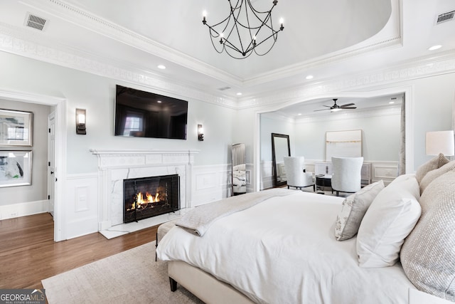 bedroom with hardwood / wood-style floors, crown molding, a notable chandelier, a tray ceiling, and a premium fireplace