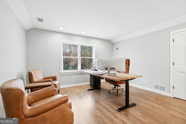 home office featuring vaulted ceiling, light hardwood / wood-style floors, and a textured ceiling