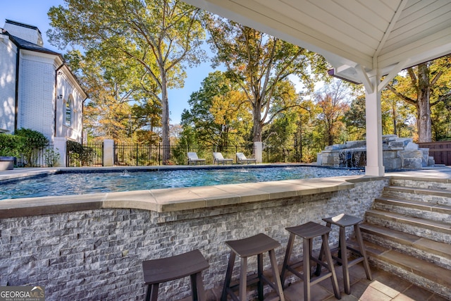 view of swimming pool with pool water feature, area for grilling, and a bar