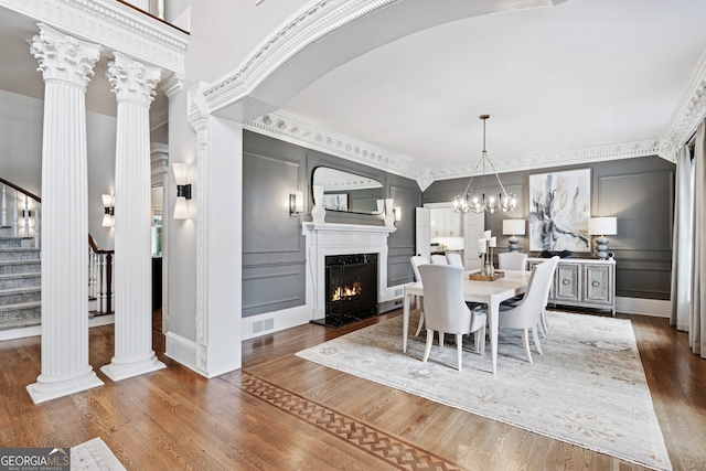 dining room featuring decorative columns, crown molding, dark wood-type flooring, and an inviting chandelier