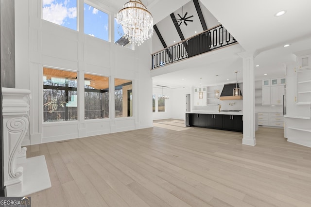 unfurnished living room featuring a notable chandelier, light wood-type flooring, decorative columns, and a high ceiling