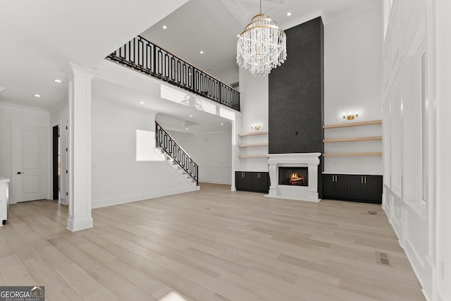 unfurnished living room with ornate columns, ornamental molding, a large fireplace, and light hardwood / wood-style floors