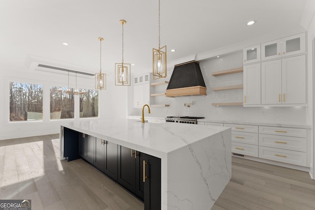 kitchen with decorative backsplash, white cabinets, custom range hood, decorative light fixtures, and a large island with sink