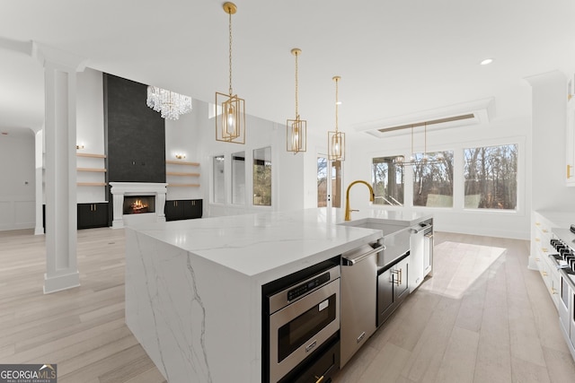 kitchen featuring pendant lighting, appliances with stainless steel finishes, light stone counters, a fireplace, and an island with sink