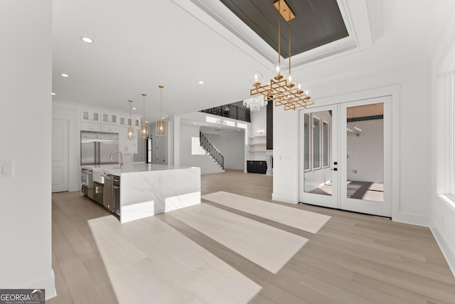 kitchen with crown molding, a center island with sink, stainless steel built in fridge, pendant lighting, and light stone countertops