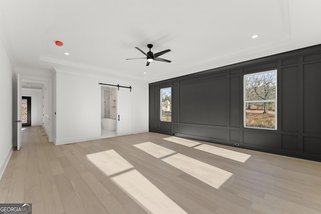 spare room with ceiling fan, a barn door, a raised ceiling, and light wood-type flooring