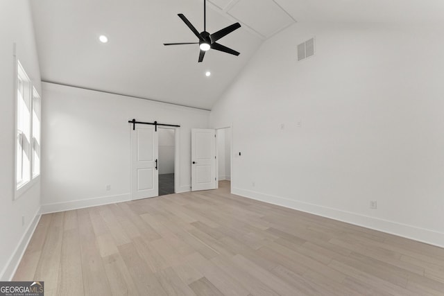 interior space featuring light wood-type flooring, a barn door, high vaulted ceiling, and a wealth of natural light