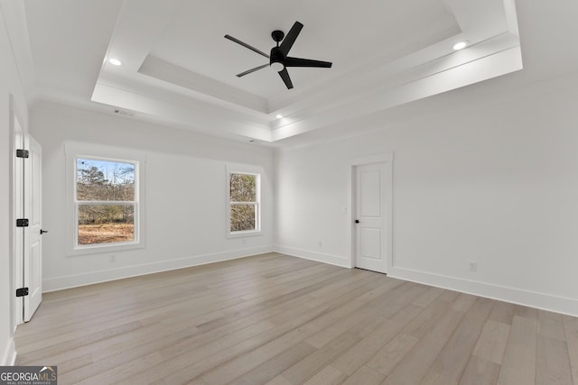 empty room featuring a raised ceiling, ceiling fan, and light hardwood / wood-style flooring