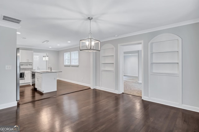 interior space with hanging light fixtures, an island with sink, white cabinets, and built in shelves