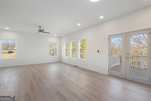 spare room with a wealth of natural light, light hardwood / wood-style flooring, french doors, and ceiling fan