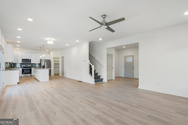 unfurnished living room with sink, ceiling fan, and light wood-type flooring