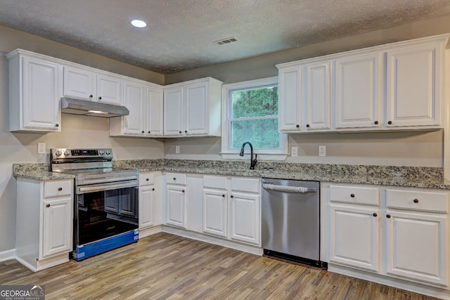 kitchen with a textured ceiling, stainless steel appliances, light stone countertops, light hardwood / wood-style floors, and white cabinets