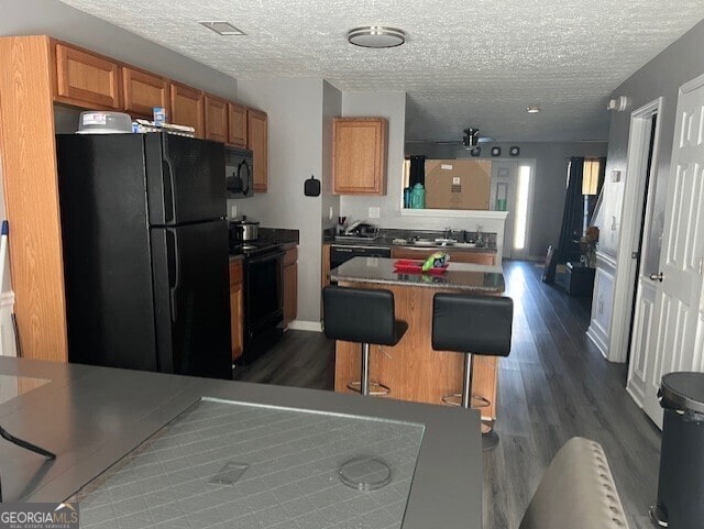 kitchen with a center island, a kitchen breakfast bar, a textured ceiling, dark wood-type flooring, and black appliances