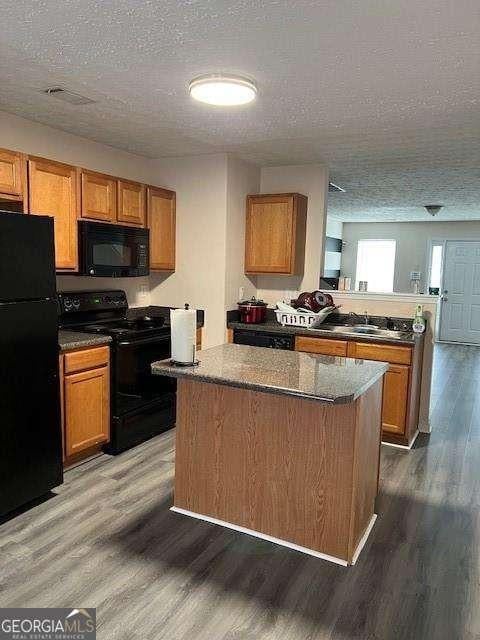 kitchen featuring sink, dark wood-type flooring, black appliances, and stone counters