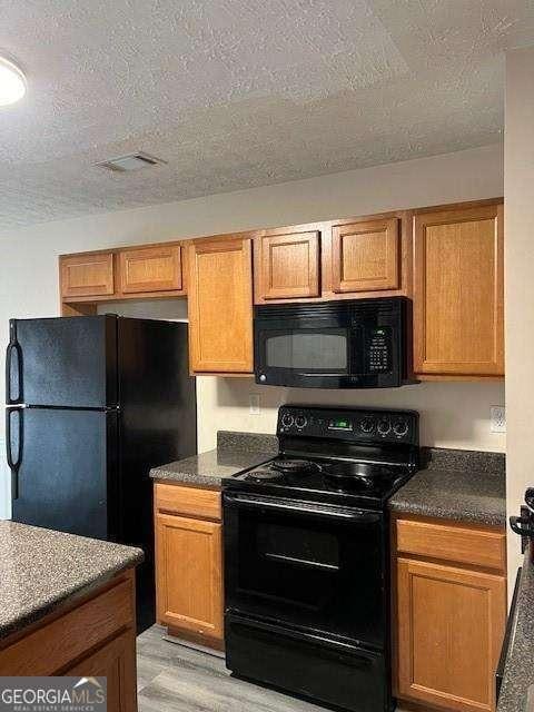 kitchen with a textured ceiling, black appliances, and light hardwood / wood-style floors