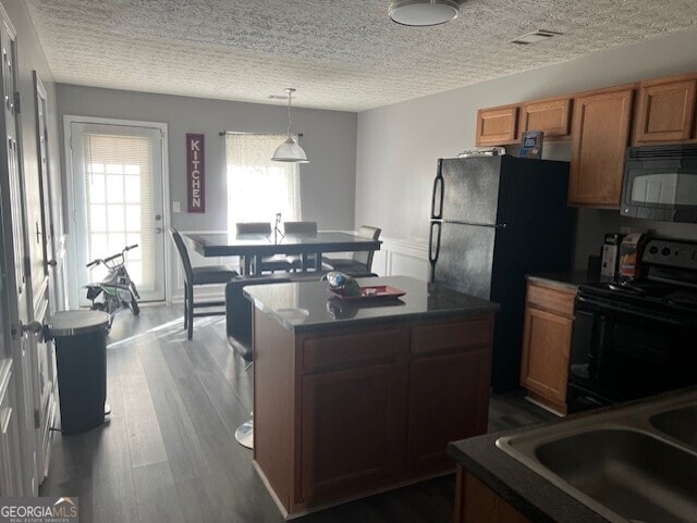 kitchen featuring wood-type flooring, sink, a kitchen island, black appliances, and hanging light fixtures