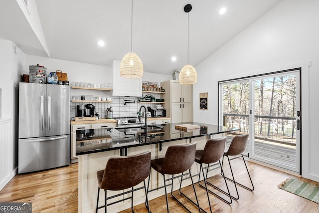 kitchen with sink, stainless steel refrigerator, a kitchen breakfast bar, decorative light fixtures, and light wood-type flooring