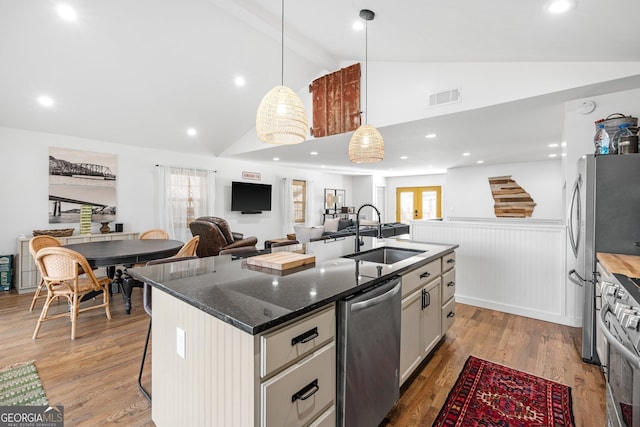 kitchen featuring sink, appliances with stainless steel finishes, a kitchen island with sink, white cabinets, and a kitchen bar