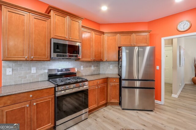 kitchen with light stone counters, stainless steel appliances, decorative backsplash, and light wood-type flooring