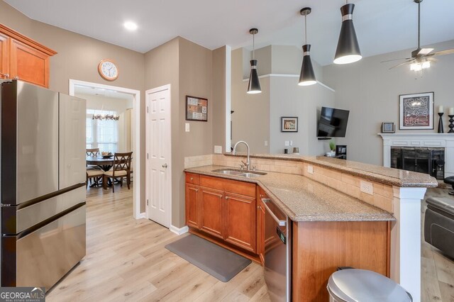 kitchen featuring pendant lighting, sink, light hardwood / wood-style flooring, dishwasher, and light stone counters