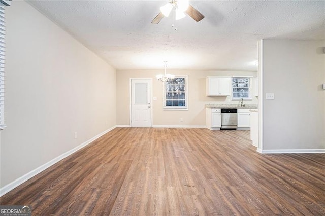 unfurnished living room featuring hardwood / wood-style flooring, ceiling fan with notable chandelier, and a textured ceiling