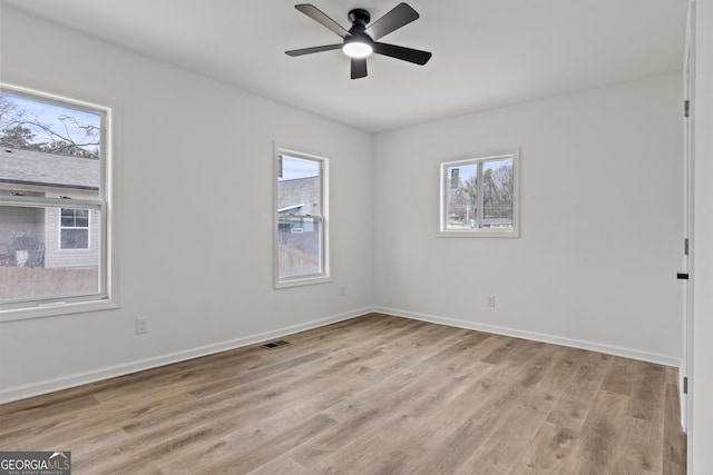 empty room with ceiling fan, a wealth of natural light, and light wood-type flooring