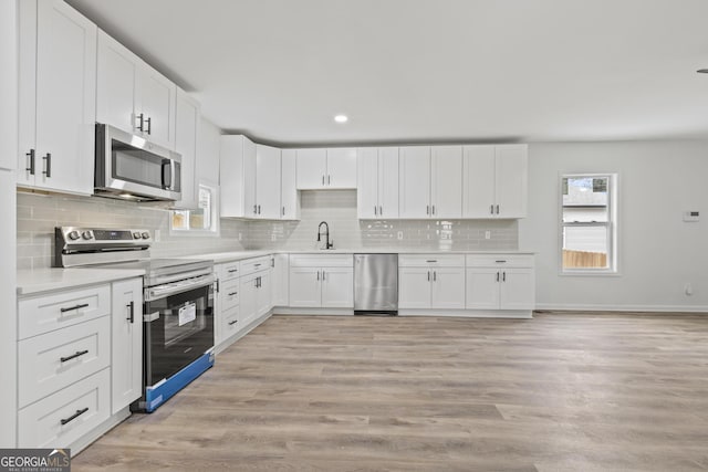 kitchen featuring sink, light hardwood / wood-style flooring, appliances with stainless steel finishes, white cabinetry, and decorative backsplash