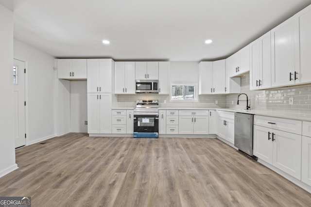 kitchen with sink, backsplash, stainless steel appliances, white cabinets, and light wood-type flooring