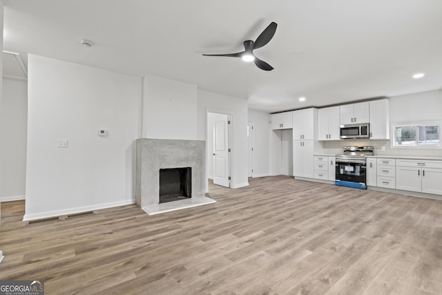 unfurnished living room featuring ceiling fan, light wood-type flooring, and a high end fireplace