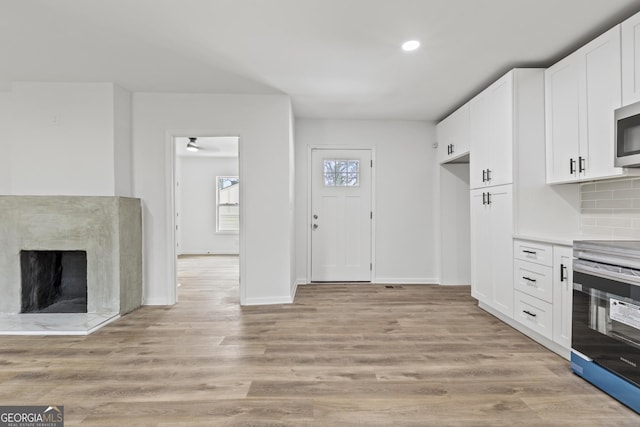 kitchen featuring appliances with stainless steel finishes, white cabinetry, tasteful backsplash, a high end fireplace, and light hardwood / wood-style floors