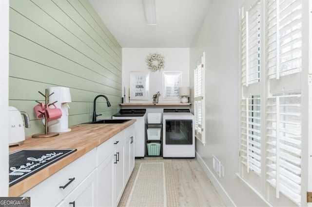 kitchen with wooden walls, butcher block counters, sink, white cabinets, and cooktop