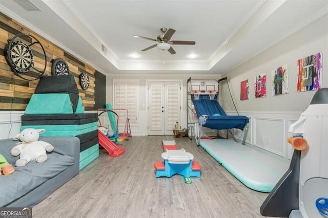 rec room with crown molding, ceiling fan, a raised ceiling, and light wood-type flooring