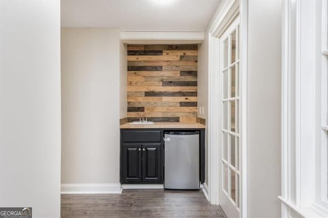 bar featuring dark wood-type flooring, wooden walls, refrigerator, and sink